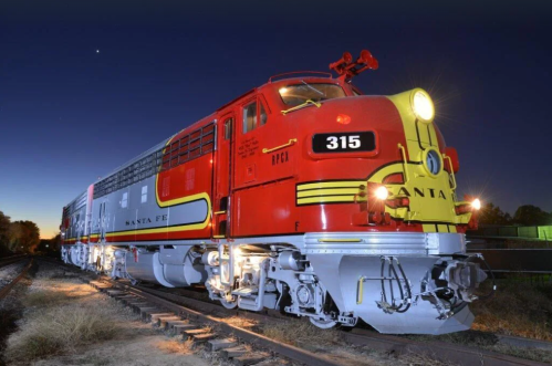 A vintage red and yellow Santa Fe locomotive parked on tracks at dusk, showcasing its classic design and vibrant colors.