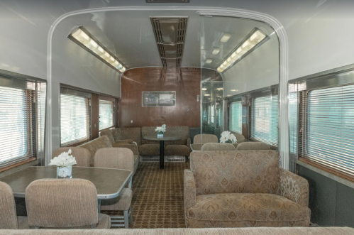 Interior of a vintage train car featuring cozy seating, tables, and large windows with natural light.