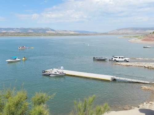 A serene lake scene with boats near a dock, surrounded by hills and a clear blue sky.