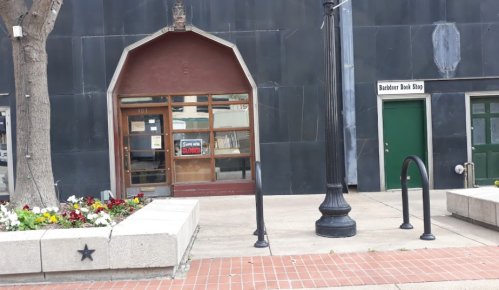 A storefront with a large archway entrance, next to a green door, and a flower bed in front.