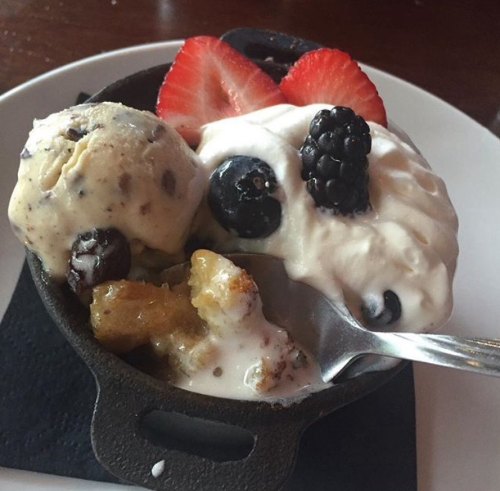 A small cast-iron dish with warm dessert, topped with ice cream, whipped cream, and fresh berries.