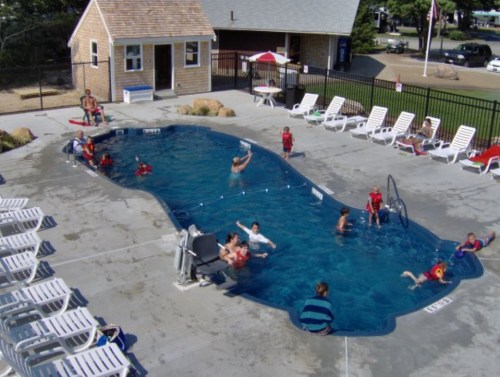 Aerial view of a pool area with children swimming, lounging chairs, and a small building in the background.