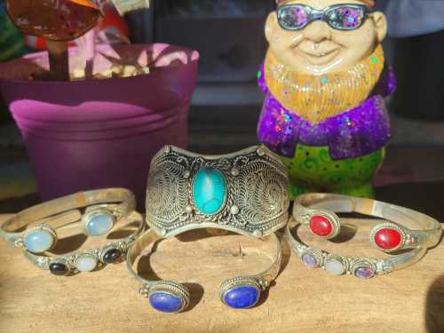 A collection of silver bracelets with colorful stones, displayed beside a decorative gnome and a potted plant.