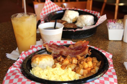 A breakfast plate with scrambled eggs, bacon, potatoes, and a biscuit, alongside iced tea and coffee.