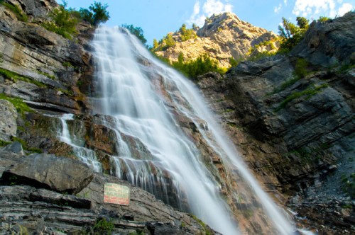 A majestic waterfall cascading down rocky cliffs, surrounded by lush greenery and a clear blue sky.