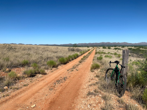A green bicycle rests beside a dirt path in a wide, open landscape with sparse vegetation and distant mountains.