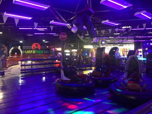 A vibrant arcade with neon lights, featuring bumper cars and a hanging figure, creating a fun atmosphere.