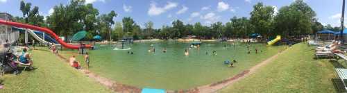 A panoramic view of a busy water park with slides, a swimming area, and people enjoying the sun and water activities.