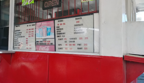Menu board displaying drinks, snacks, and ice cream prices at a food stand, with Coca-Cola branding visible.