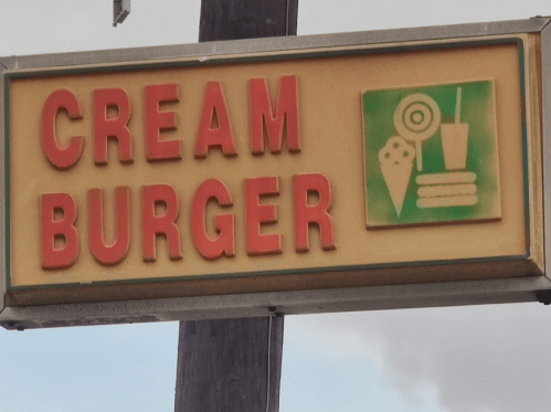 Sign for "Cream Burger" featuring ice cream, a drink, and a burger icon. Bright red letters on a yellow background.