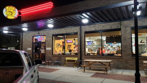 Exterior of Busy Bee Cafe at night, featuring bright signage, open windows, and outdoor seating.
