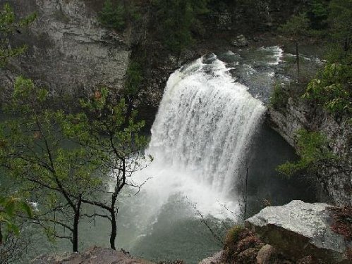 A cascading waterfall flows into a serene pool, surrounded by rocky cliffs and lush greenery.
