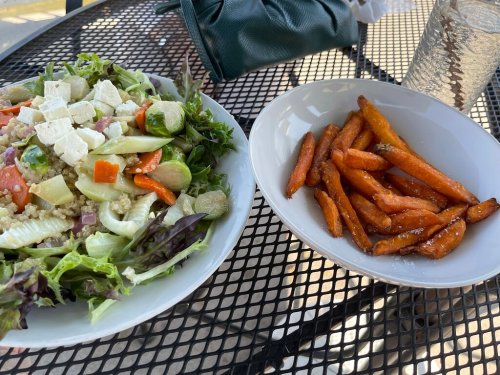 A fresh salad with feta cheese and a side of sweet potato fries on a black metal table.
