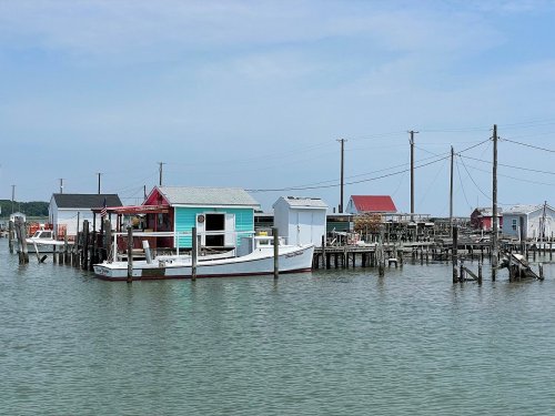 Colorful houses on stilts by the water, with boats and utility poles in a serene coastal setting.