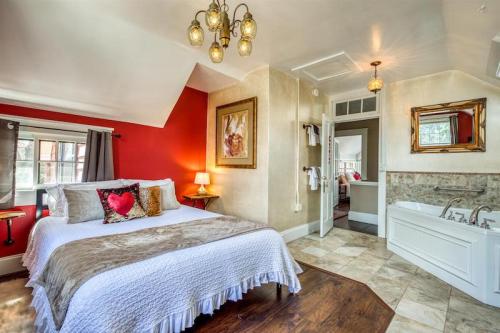 Cozy bedroom with a white bed, red accent wall, chandelier, and an en-suite bathroom visible in the background.
