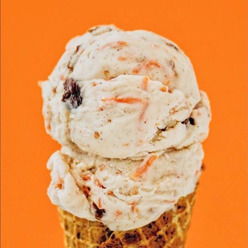 A close-up of a scoop of carrot cake ice cream on a waffle cone against an orange background.