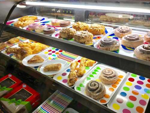 A display case filled with various pastries, including cinnamon rolls, donuts, and croissants on colorful plates.