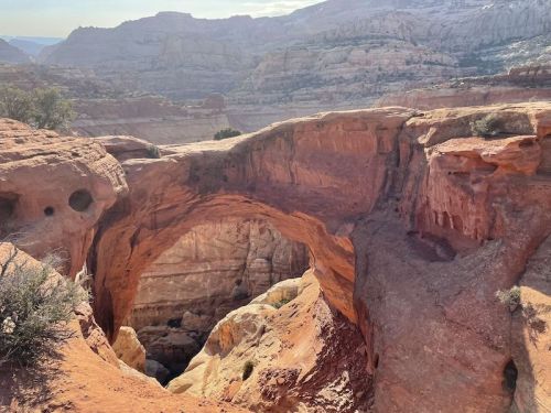 A natural rock arch in a rugged desert landscape, surrounded by layered red and beige rock formations.