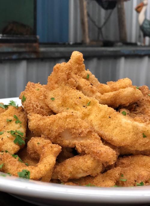 A close-up of a plate piled high with golden-brown, crispy fried fish fillets, garnished with parsley.