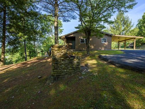 A rustic house surrounded by trees, featuring a stone structure in the foreground and a driveway leading up to it.