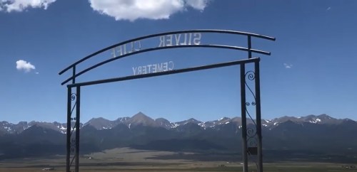 A metal archway reading "Silver Cliff Cemetery" with mountains and a blue sky in the background.