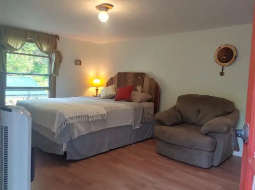 Cozy bedroom with a bed, a chair, a lamp, and a window, featuring warm lighting and simple decor.