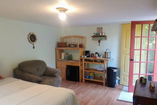 Cozy room with a bed, a sofa, a wooden shelf, and a bright yellow door leading outside.