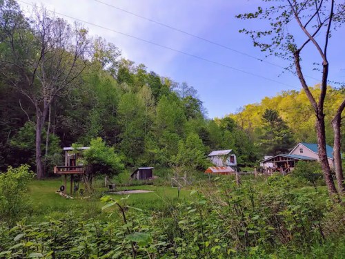 A serene landscape featuring small buildings surrounded by lush greenery and trees under a clear blue sky.