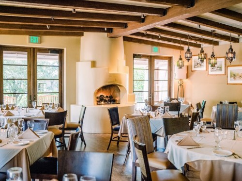 Cozy restaurant interior with wooden beams, elegant tables, and a fireplace, creating a warm dining atmosphere.