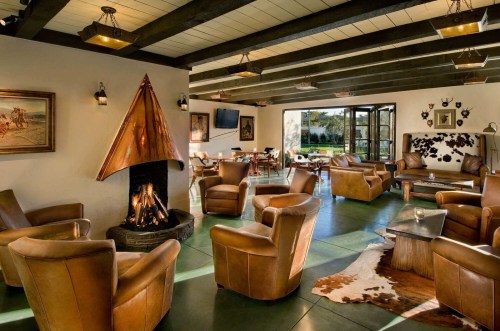 Cozy lounge with leather chairs, a fireplace, and large windows overlooking a scenic view. Warm, inviting atmosphere.