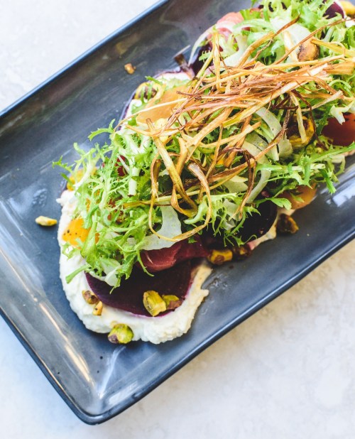 A colorful salad with layers of beets, greens, and crispy toppings on a dark plate.