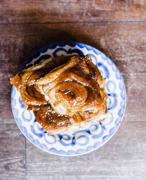 A blue and white patterned plate stacked with golden-brown cinnamon rolls, lightly dusted with powdered sugar.