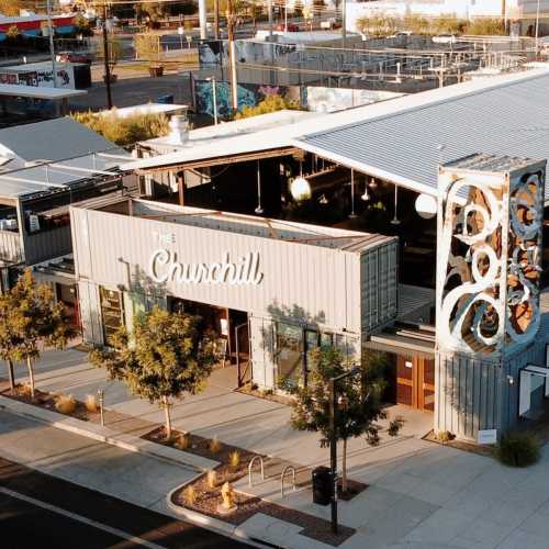 Aerial view of The Churchill, a modern building with outdoor seating and greenery in a vibrant urban setting.