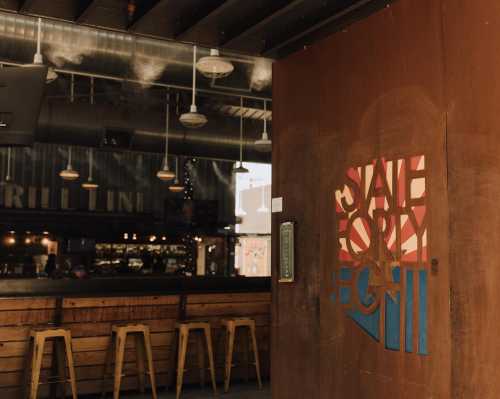 A rustic bar entrance with a colorful state-themed sign and wooden stools in a modern interior setting.