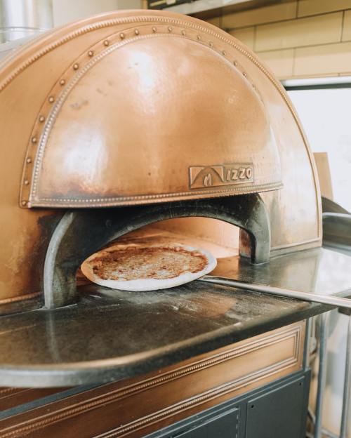 A freshly baked pizza is being pulled from a copper pizza oven.