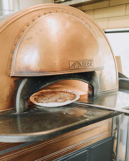 A freshly baked pizza is being pulled from a copper pizza oven.