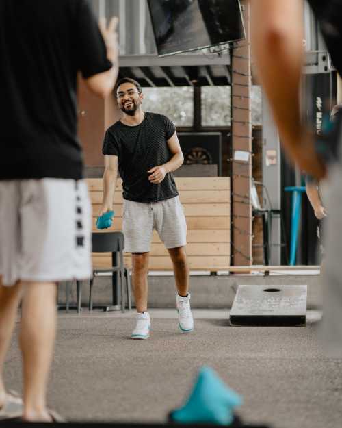 A smiling man in a black shirt and gray shorts plays a game outdoors, engaging with others in a casual setting.