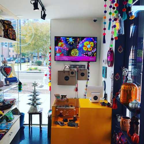 A colorful boutique interior featuring decorative items, a TV screen, and vibrant tassels hanging from the ceiling.