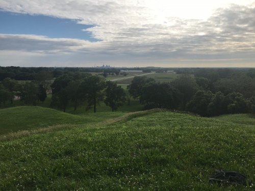 A scenic view of rolling green hills with a distant city skyline under a cloudy sky.