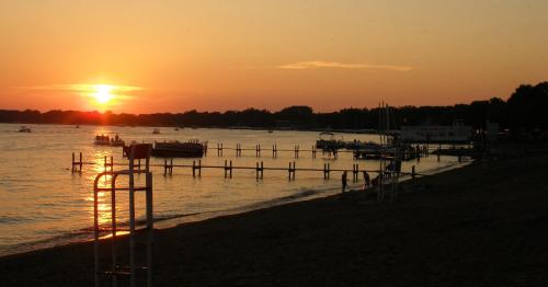 Sunset over a calm beach with boats on the water and silhouettes of trees in the background.