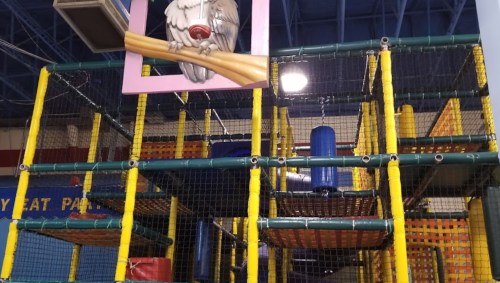 Colorful indoor play structure with nets, tubes, and a cartoon owl decoration on the wall above.