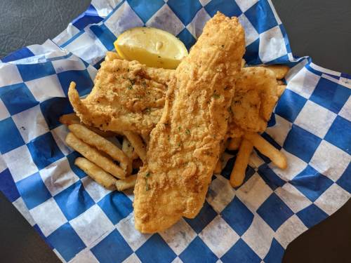 A plate of golden fried fish fillets with a lemon wedge, served with crispy French fries on a blue and white checkered paper.