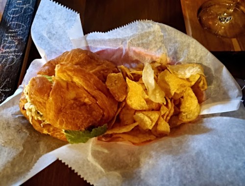 A croissant sandwich with lettuce and a side of potato chips, served on parchment paper.