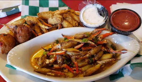 A plate of seafood featuring crab claws, fried fish, hushpuppies, and dipping sauces on a red table.