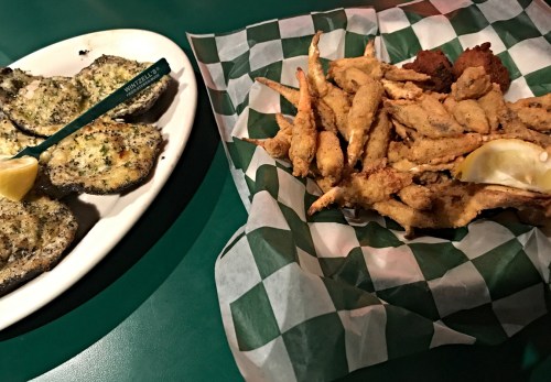 A plate of baked oysters with lemon and a basket of fried seafood on a green checkered tablecloth.