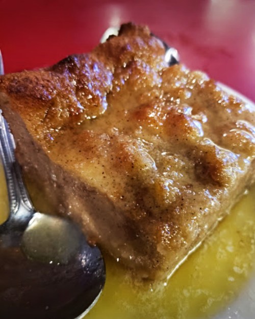A close-up of a golden-brown dessert with a glossy glaze, served on a plate with a spoon beside it.