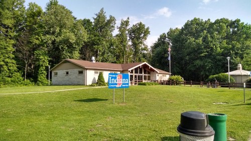 A building surrounded by trees with a sign that reads "Welcome to Indiana" in front, on a grassy area.