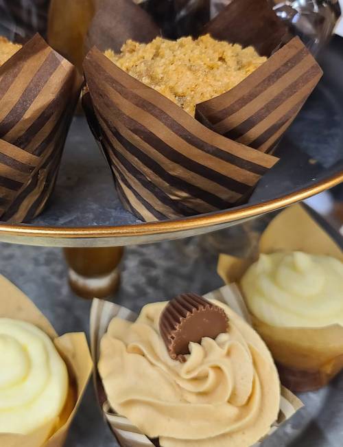 A tiered display of cupcakes: two brown muffins on top and two cream-colored cupcakes with swirls and a chocolate piece below.