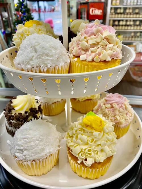 A tiered display of colorful cupcakes topped with various frosting designs, including swirls and shavings.