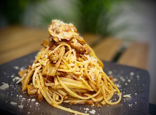 A serving of spaghetti topped with meat, cheese, and herbs, presented on a black plate with a blurred background.